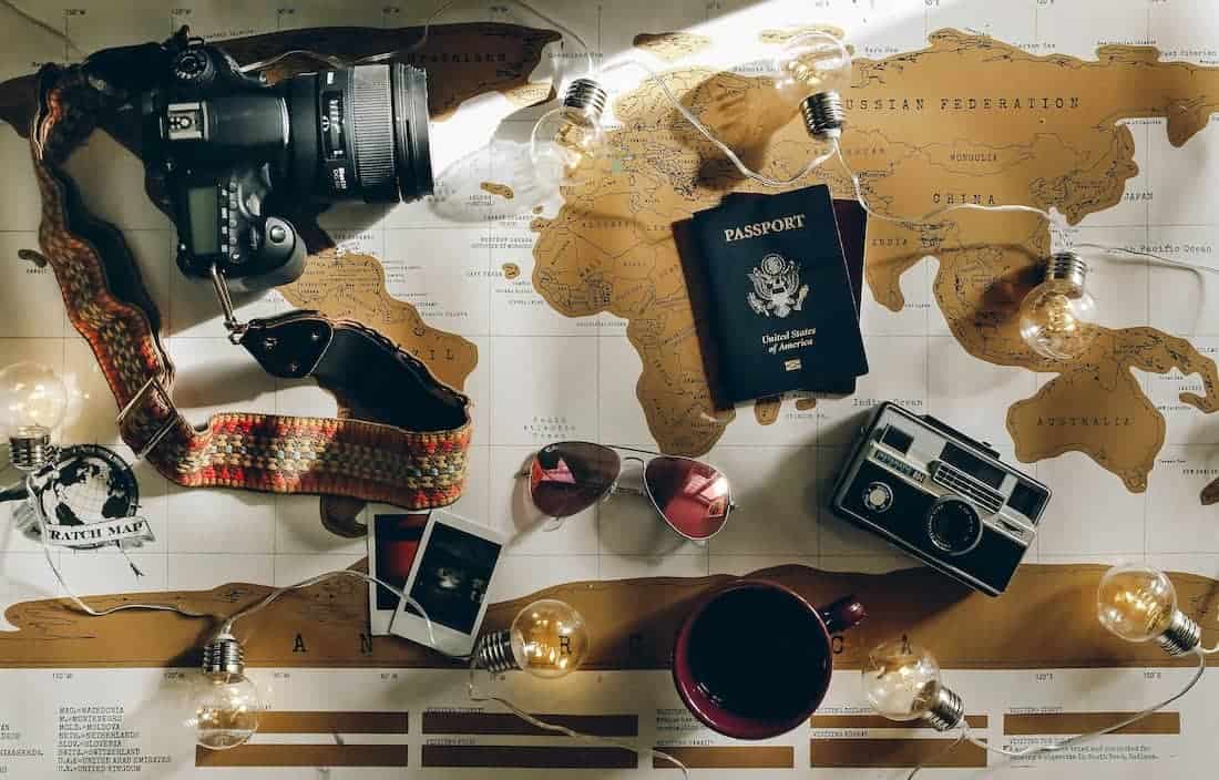 black DSLR camera near passport and other travel items like sunglasses, all on top of a world map.